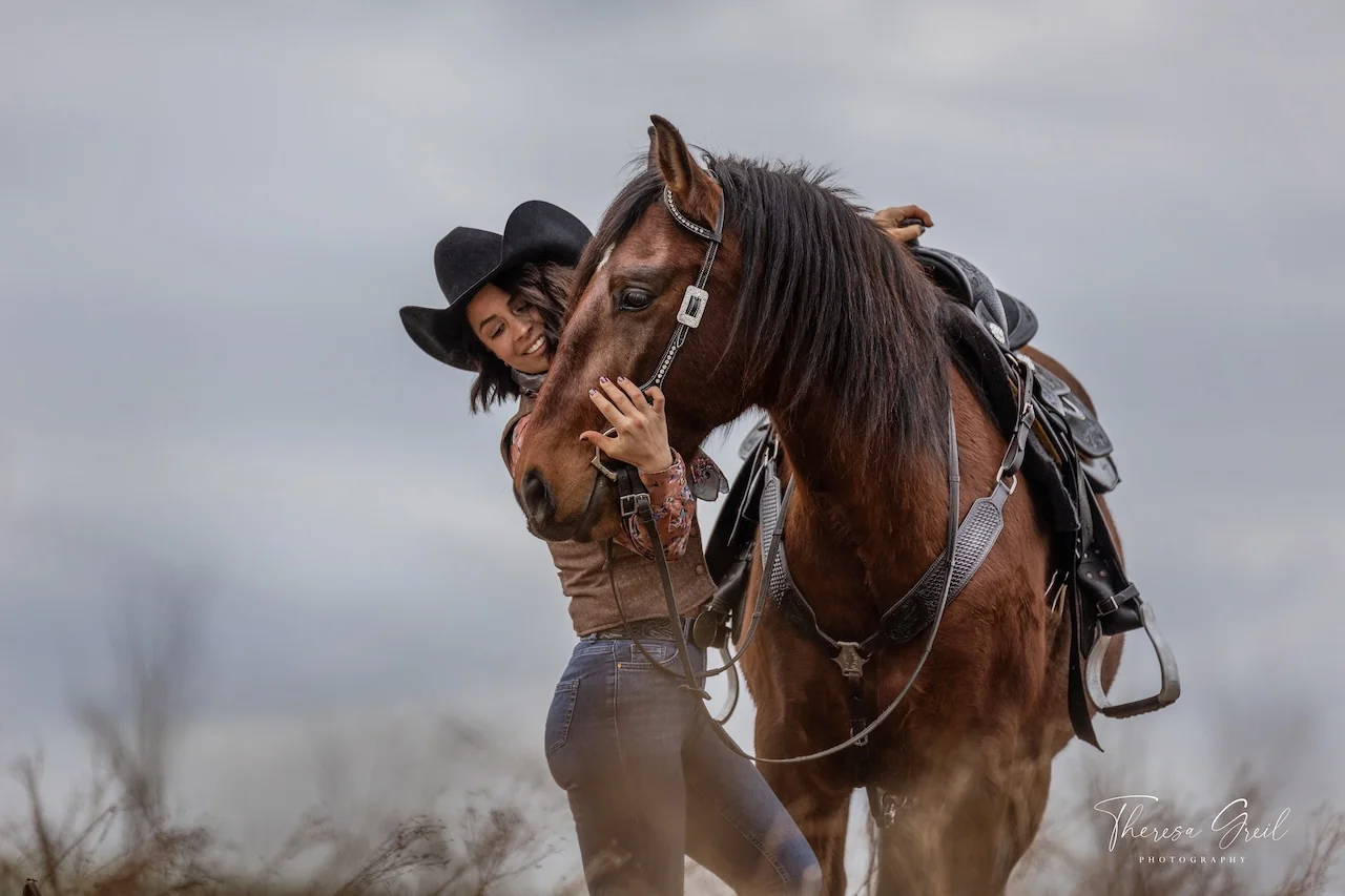 Selina Hempel mit Cowboyhut umarmt ein braunes Pferd mit Westernsattel auf der Laurent Ranch