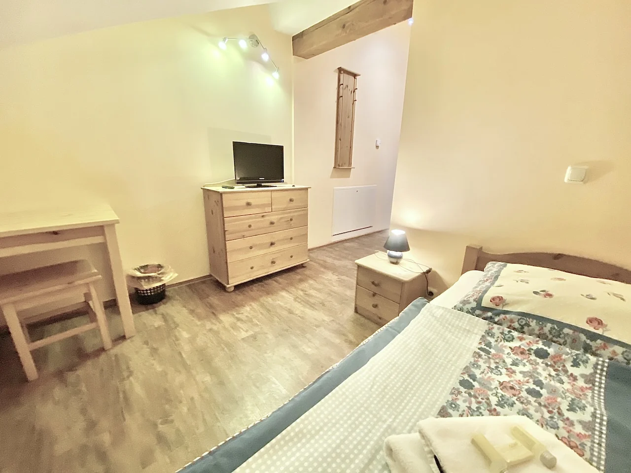 Einzelzimmer auf der Laurent Ranch in Gottfrieding mit Bett, Nachttisch und Kommode mit Fernseher unter Holzbalken