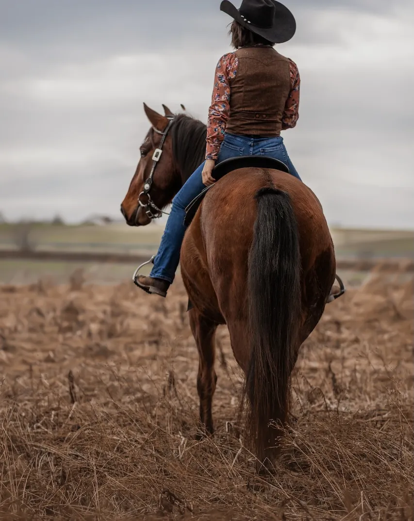 Selina Hempel mit Cowboyhut zu Pferd im abgeernteten Feld bei der Laurent Ranch in Niederbayern