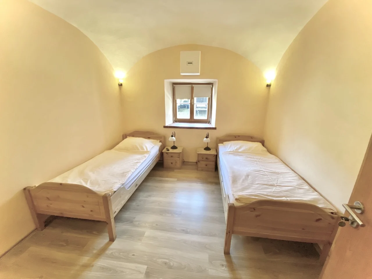 Zweibettzimmer auf der Laurent Ranch in Gottfrieding mit zwei weißen Holzbetten unter der Gewölbedecke und zwei Nachttischen