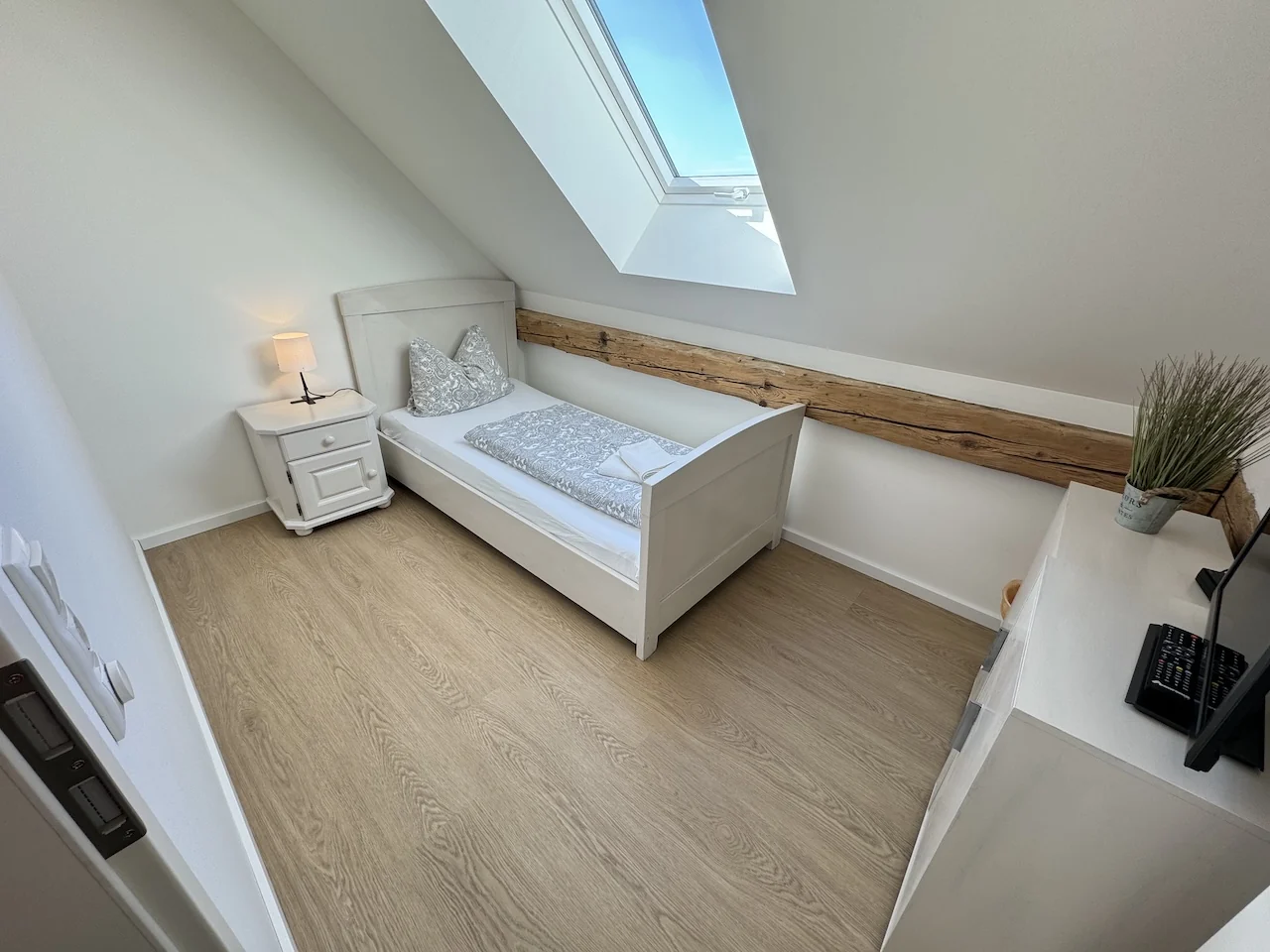 Einzelzimmer auf der Laurent Ranch in Gottfrieding mit weißem Bett, Dachfenster und Holzbalken unter der Dachschräge