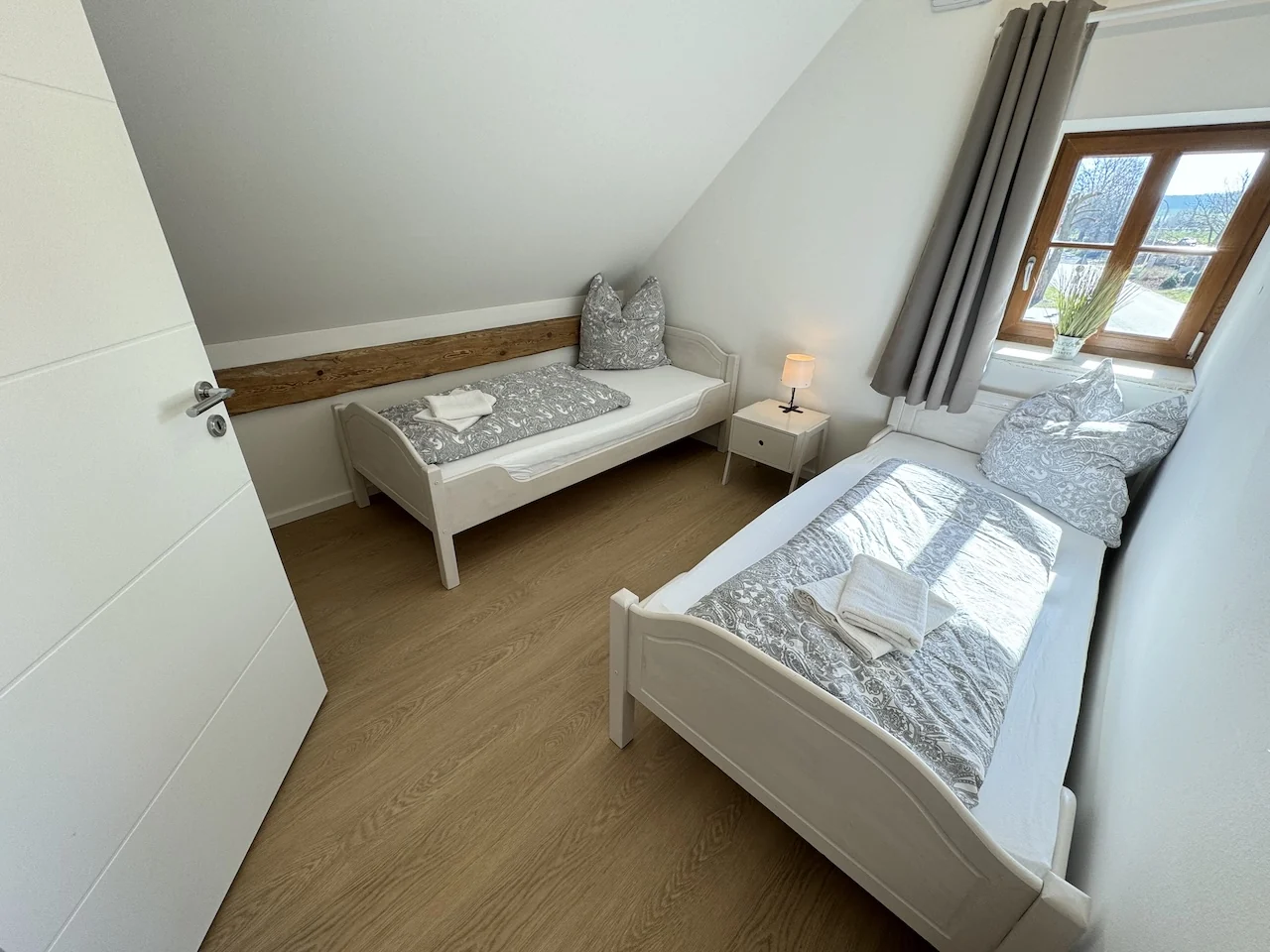 Zweibettzimmer im Apartment der Laurent Ranch in Gottfrieding mit zwei weißen Betten, Nachttisch und Holzbalken