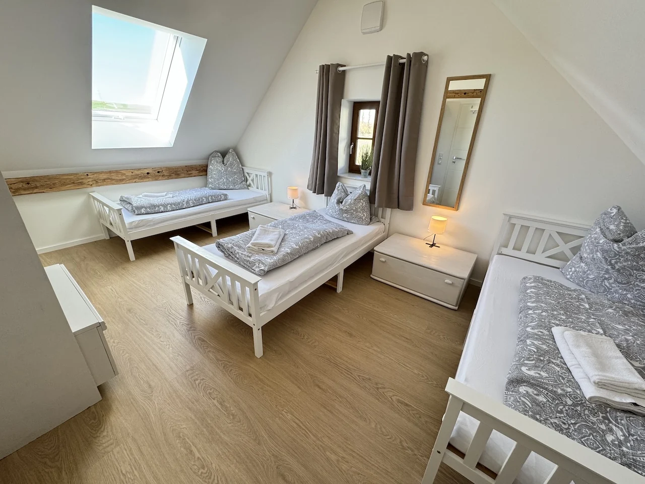 Dreibettzimmer im Apartment der Laurent Ranch in Gottfrieding mit drei weißen Holzbetten unter der Dachschräge